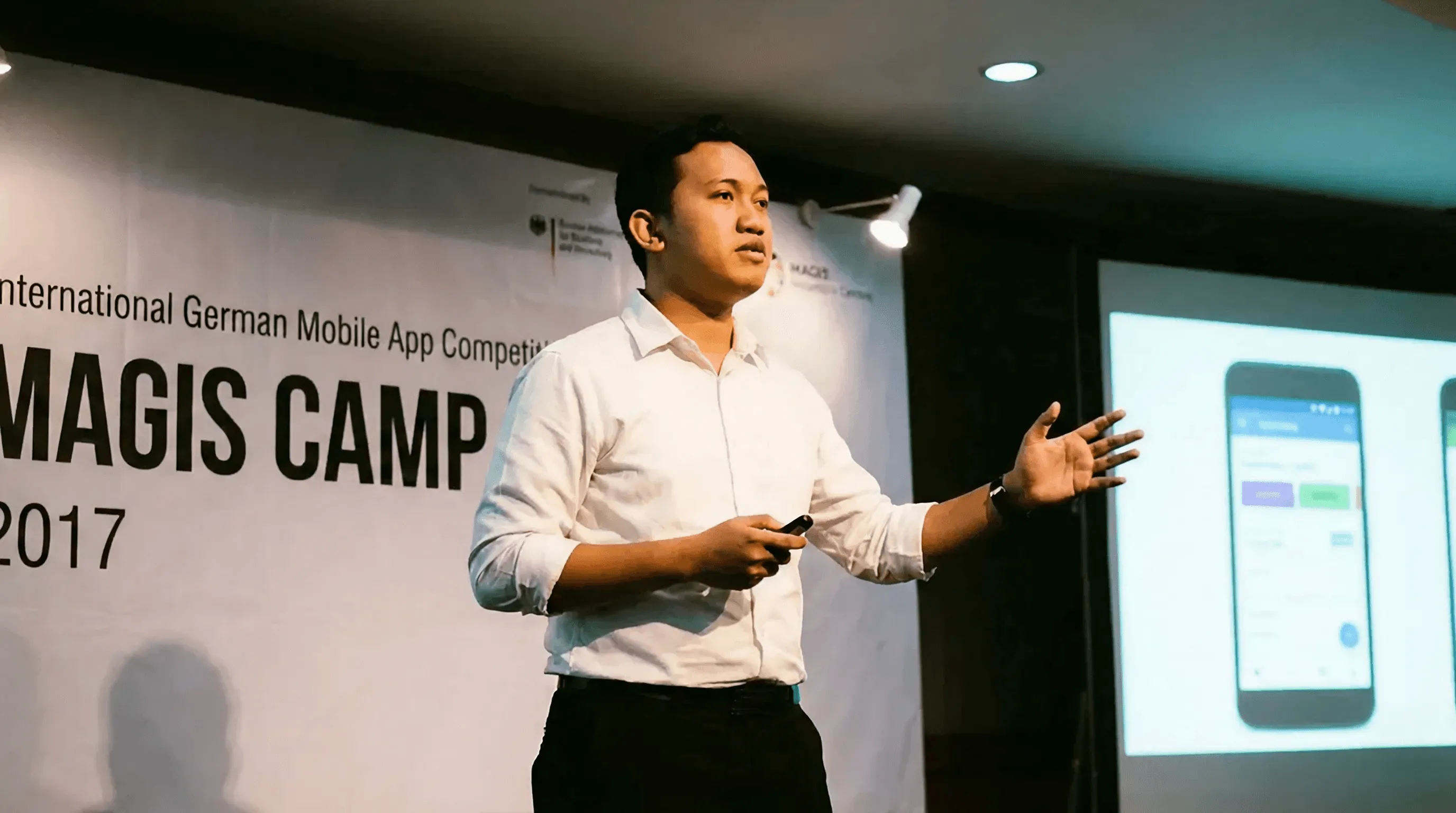 person discussing while standing in front of a large screen in front of people inside dim-lighted room